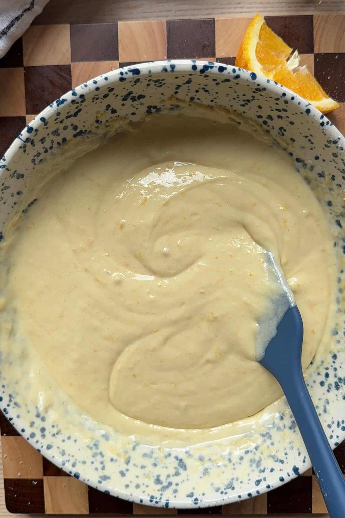 Orange cupcake batter in a bowl with a rubber spatula.