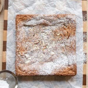 Almond croissant blondies dusted with powdered sugar on a piece of parchment paper.
