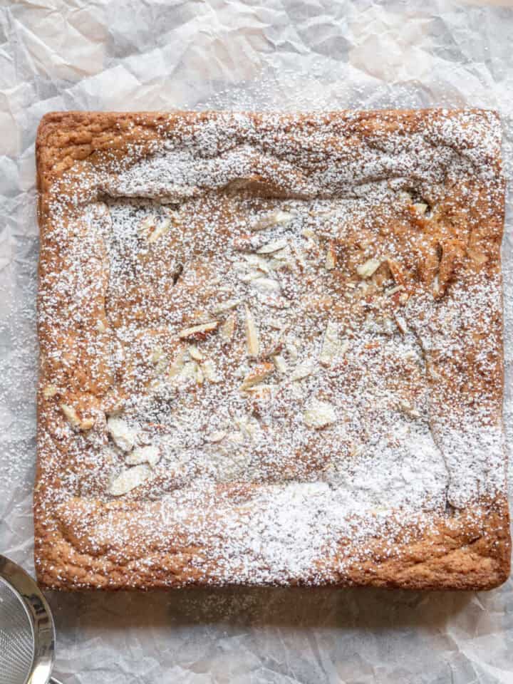 Almond croissant blondies dusted with powdered sugar on a piece of parchment paper.