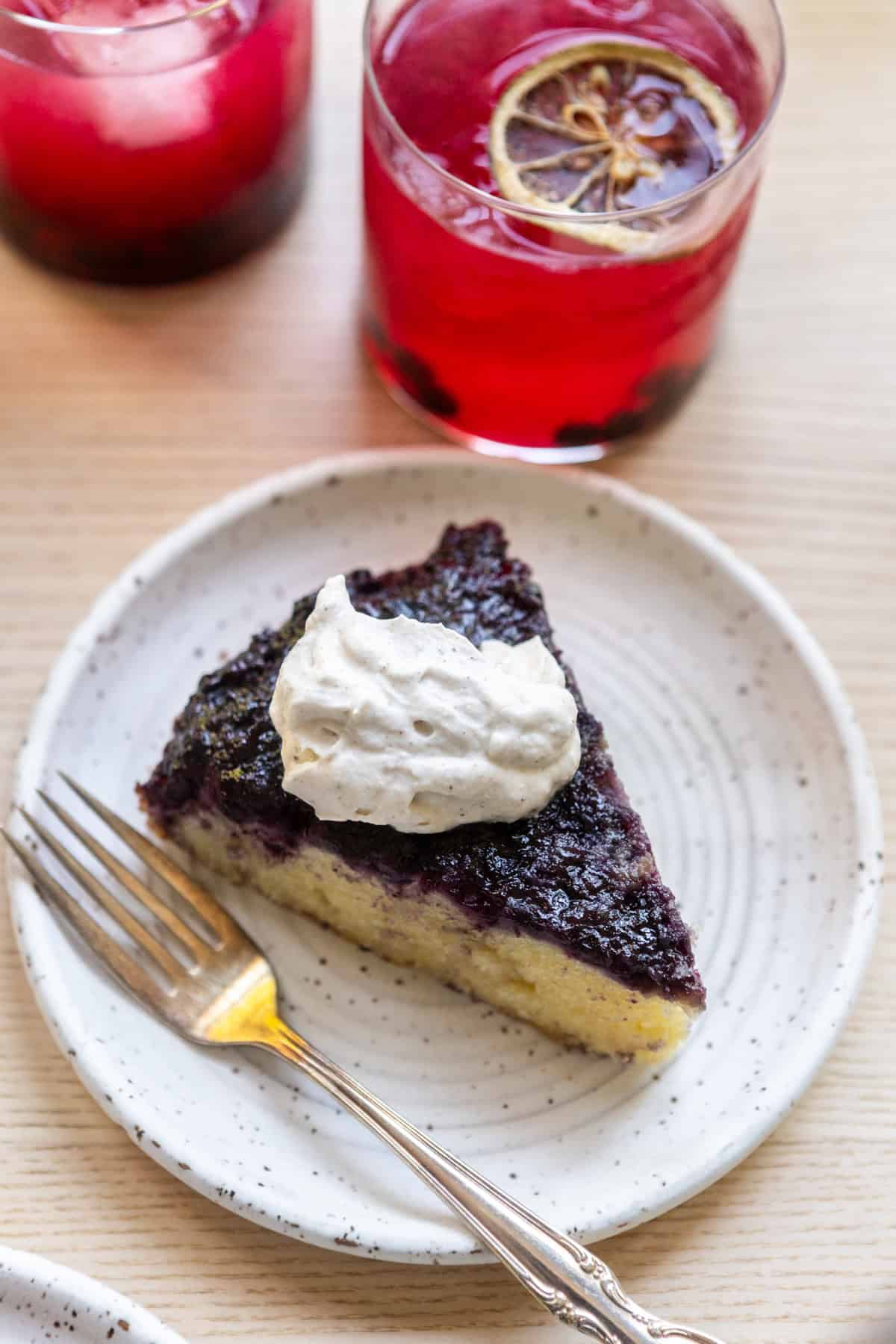 A slice of blueberry upside down cake on a white plate with whipped cream.