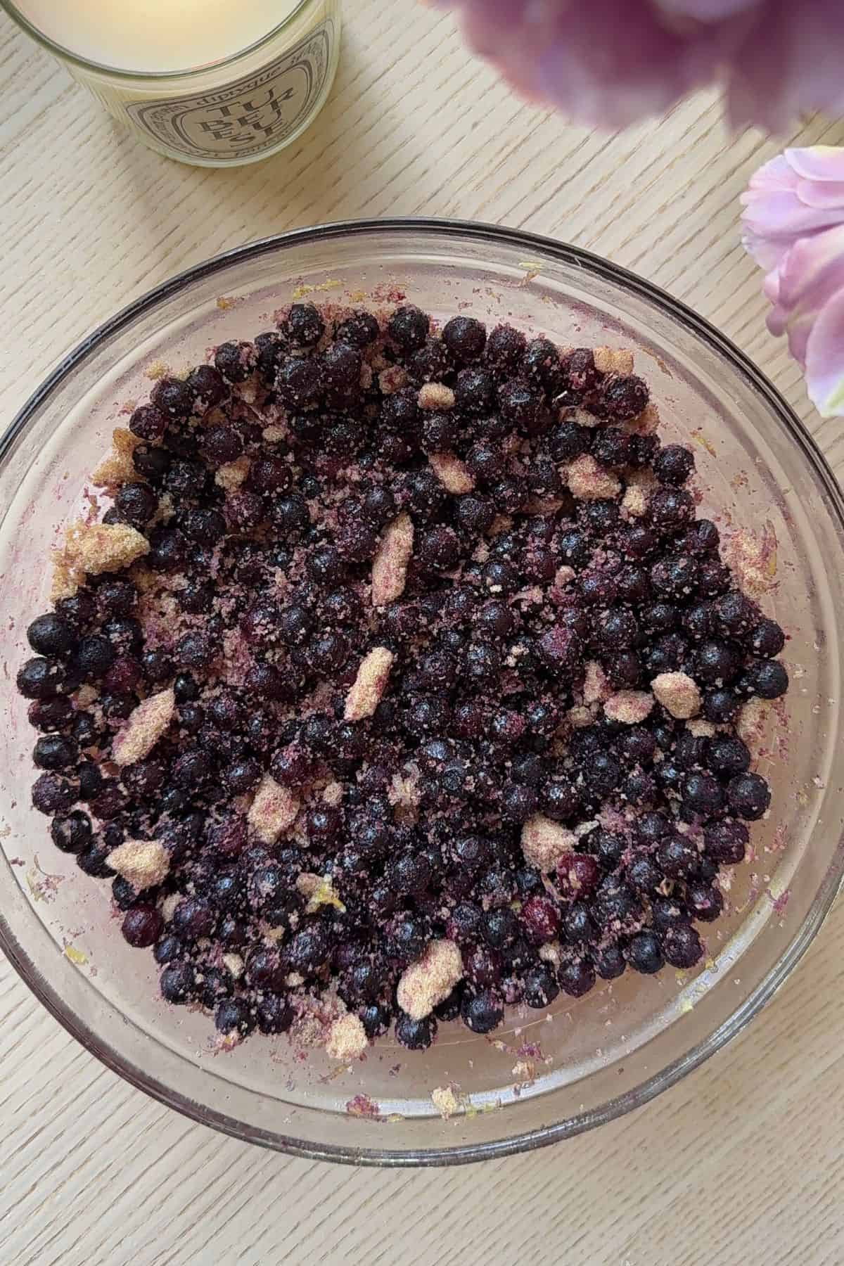 Frozen blueberries, lemon zest, and brown sugar combined in a bowl.