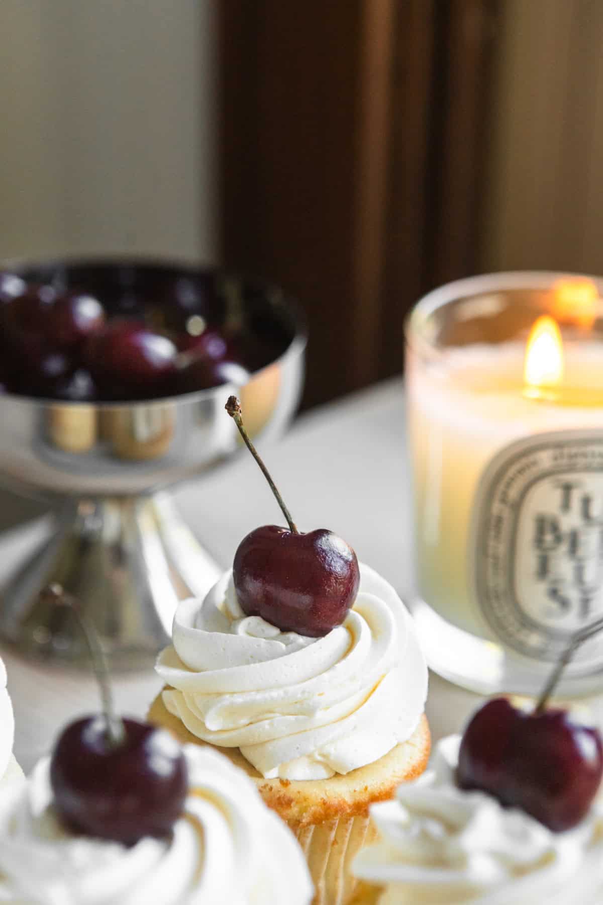 Cupcakes topped with fresh cherries on a table with a candle in the background.