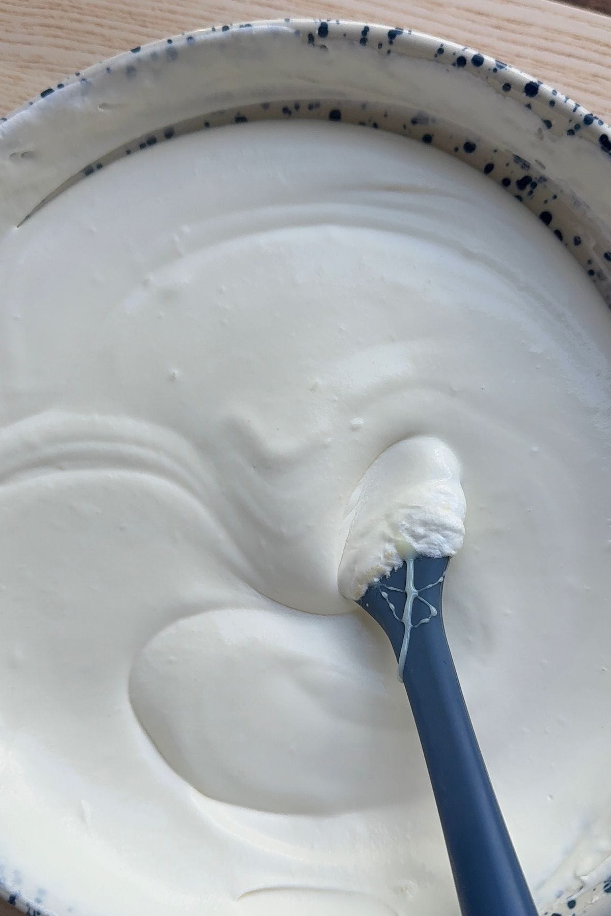 Whipped cream mixed with sweetened condensed milk in a bowl with a spatula.