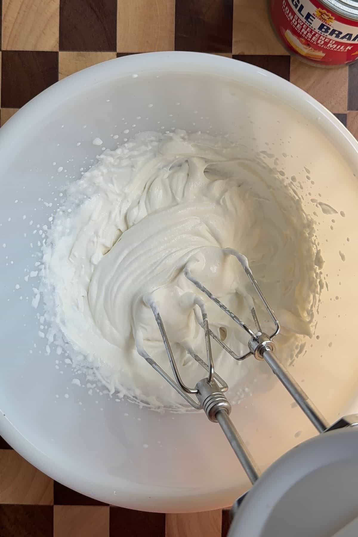 Whipped cream in a mixing bowl with a hand mixer.
