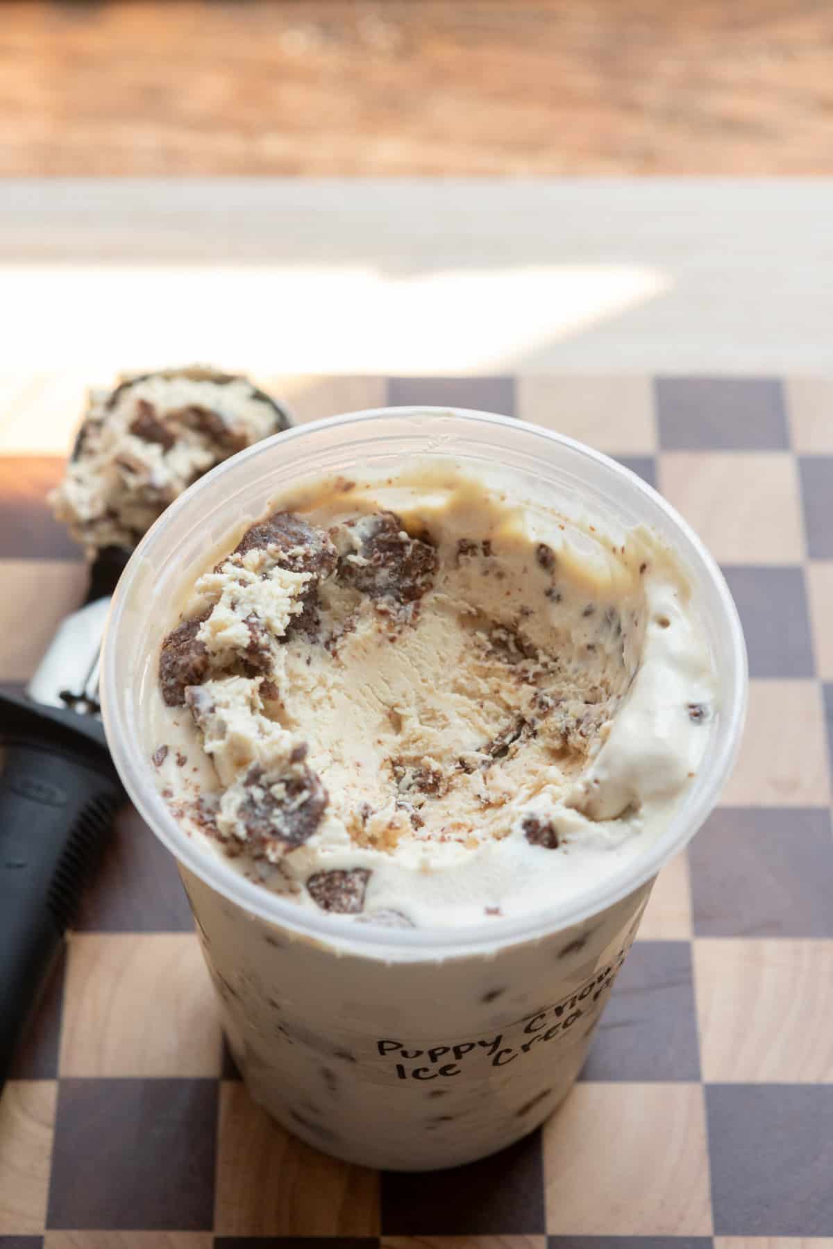 A deli container of puppy chow ice cream open on a checkered cutting board.