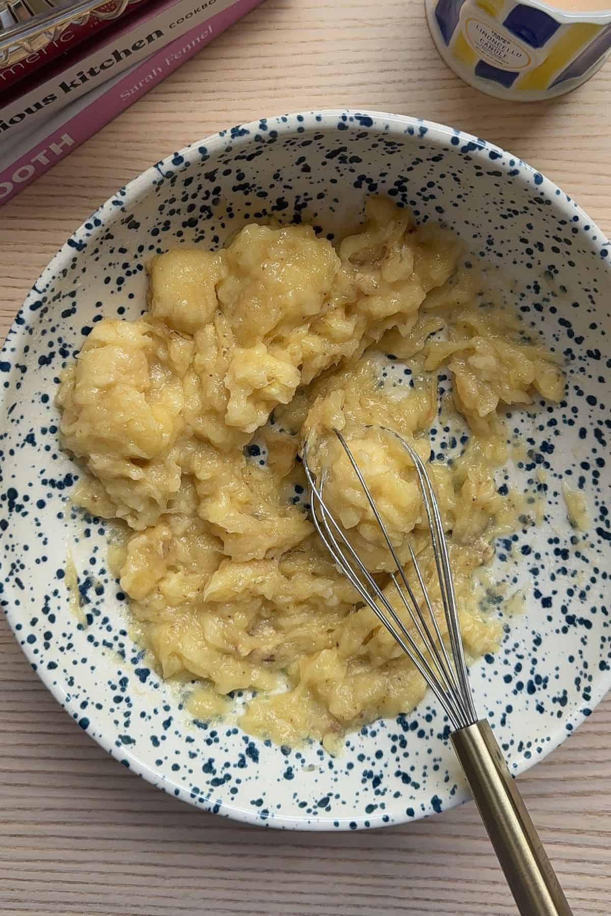Mashed bananas in a bowl with a whisk.
