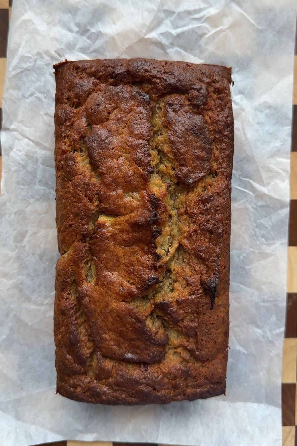 Baked banana bread on a parchment lined cutting board.