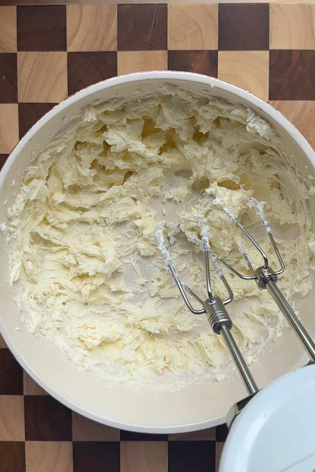 Butter and cream cheese beat together in a bowl with an electric mixer.