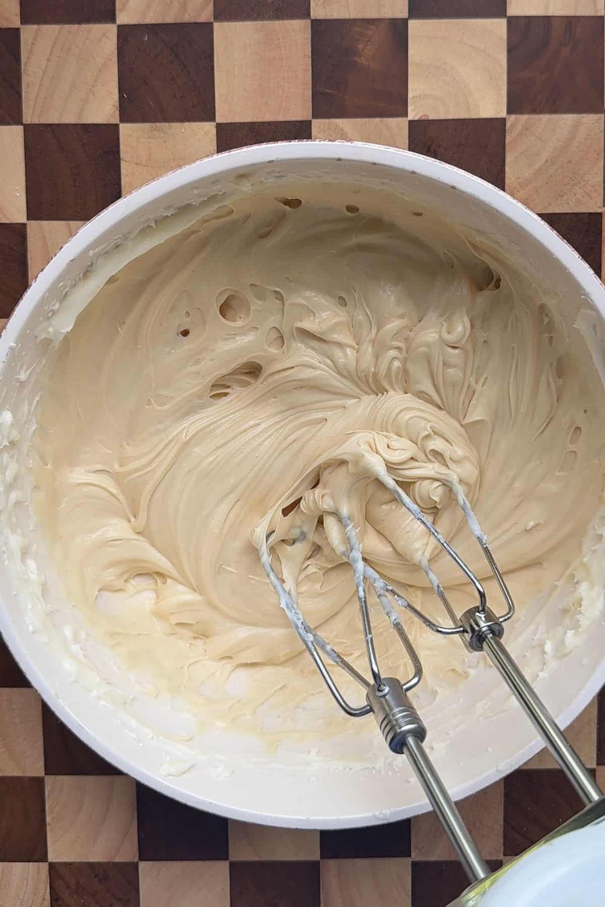 Salted caramel cream cheese frosting in a white bowl with electric mixer beaters.