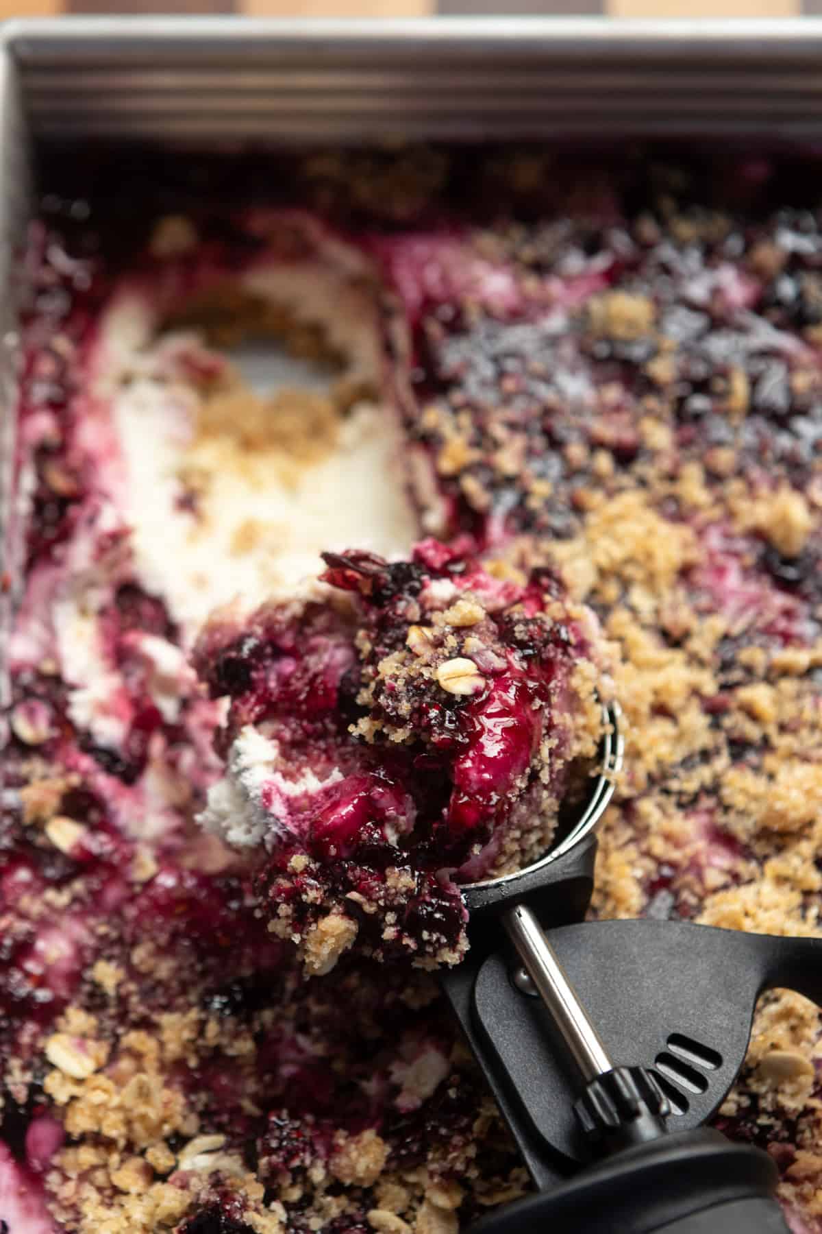 Scoopable berry cheesecake with a cookie scoop in the pan.