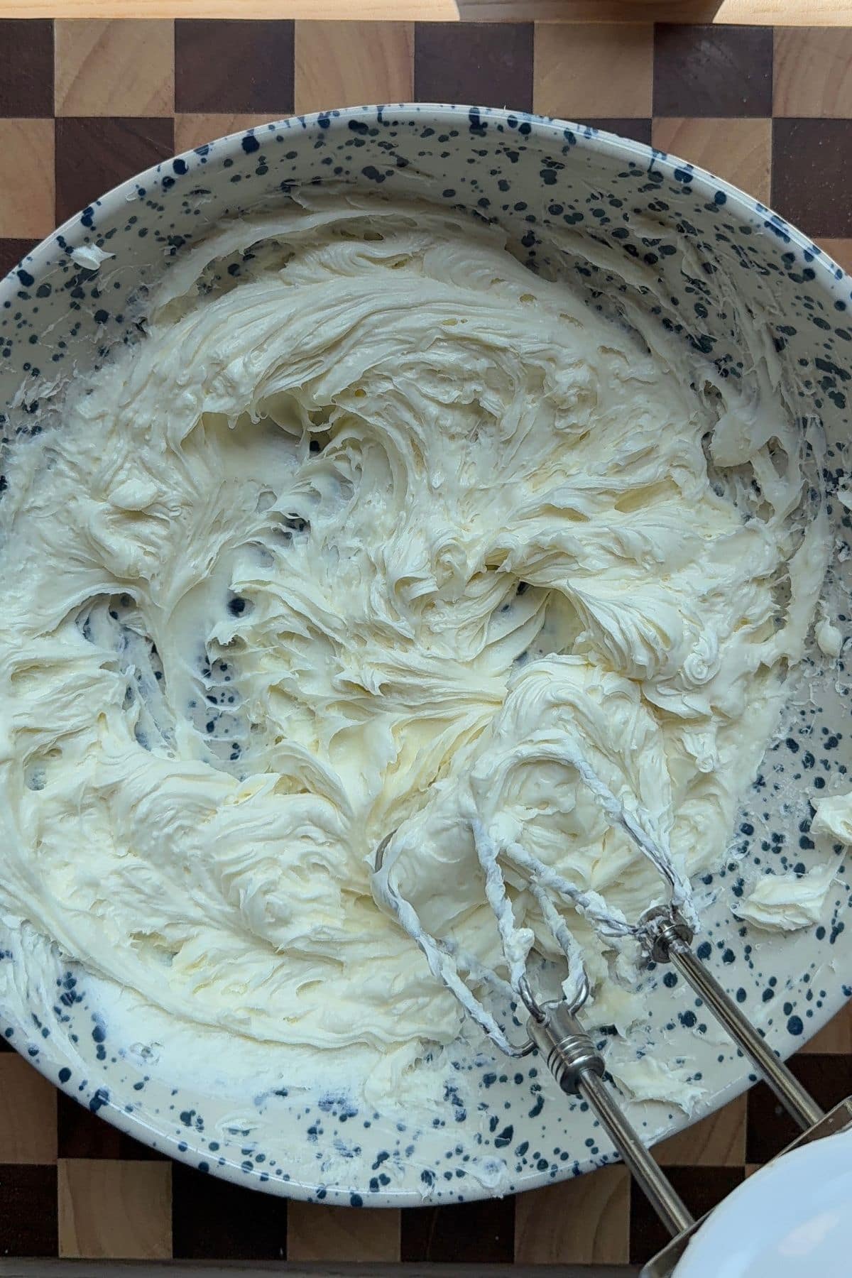 Mixing cream cheese and yogurt together in a large bowl with a handheld mixer.