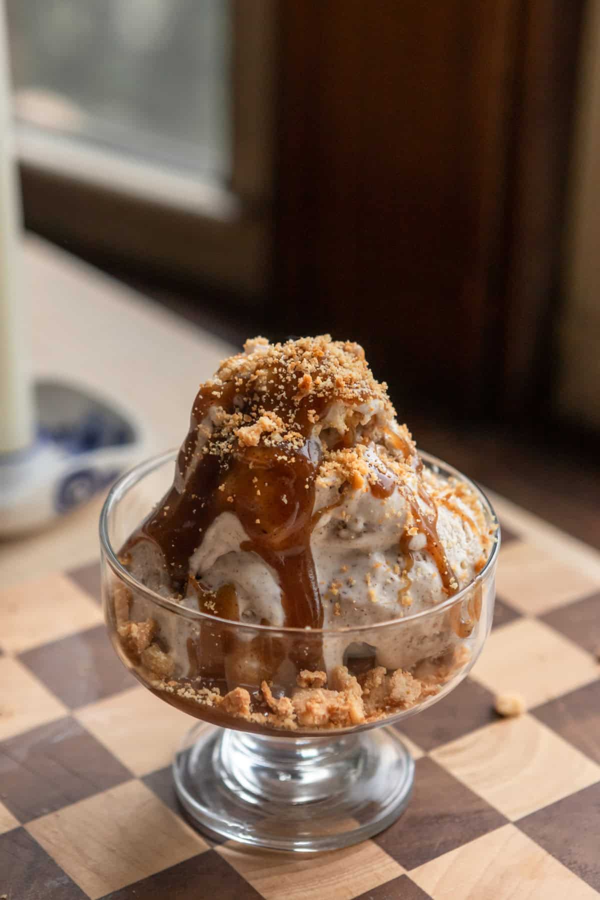 Scoops of ice cream in a glass bowl with butterscotch and pie crust crumbs.