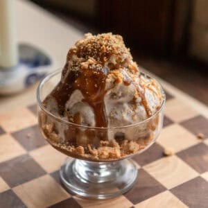 Scoops of brown sugar pop tart ice cream in a glass bowl with butterscotch and pie crust crumbs on top.