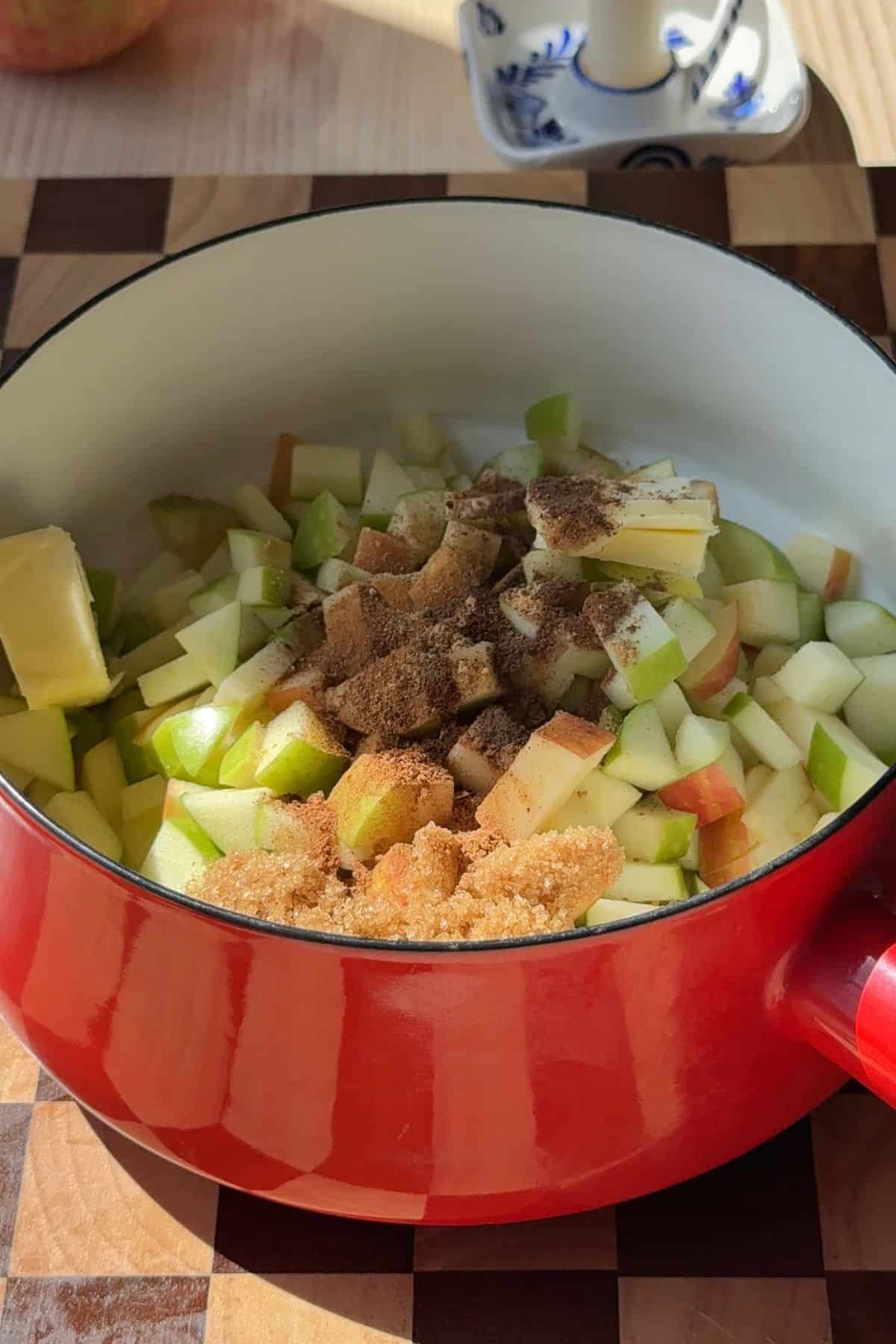 Chopped apples and spices in a red saucepan.