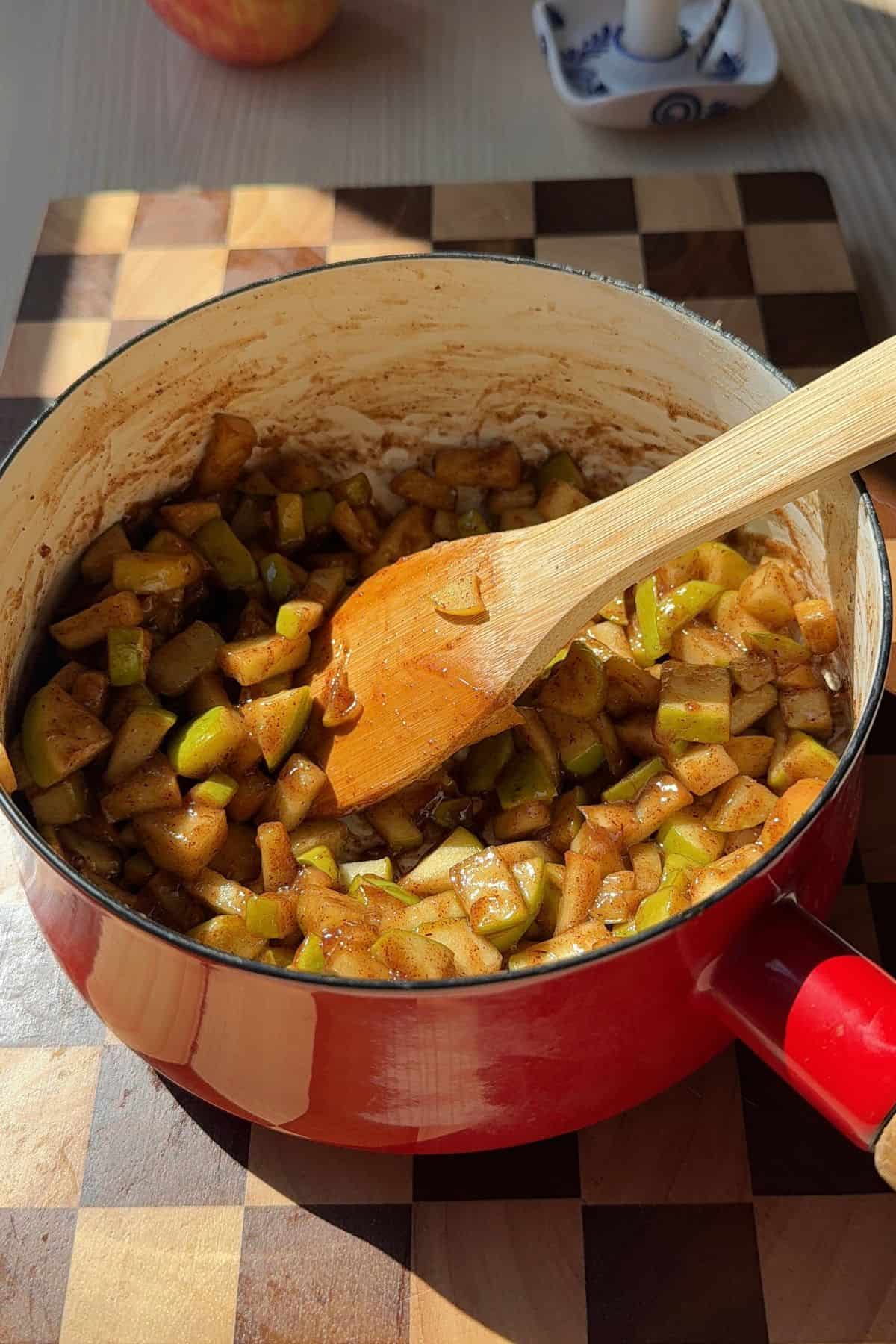 Apple pie filling in a saucepan with a wooden spoon.
