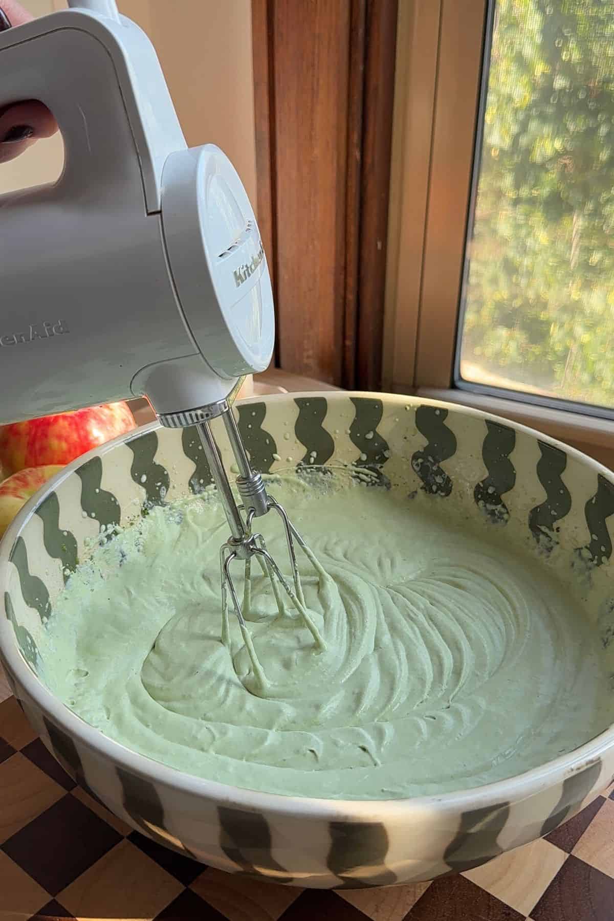 Whipped cream and matcha mixed together in a bowl with a handheld mixer.