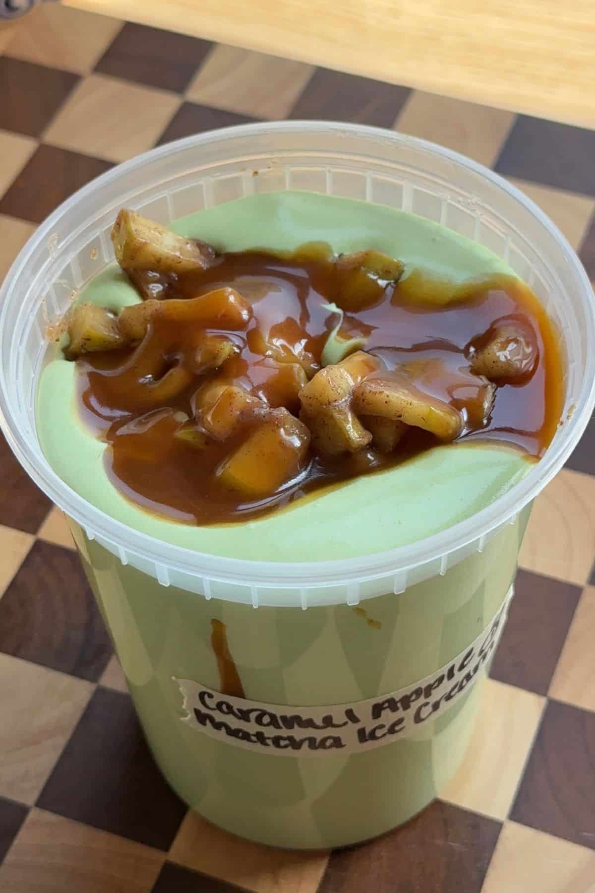 Matcha ice cream base layered with caramel sauce and apples in a deli container.