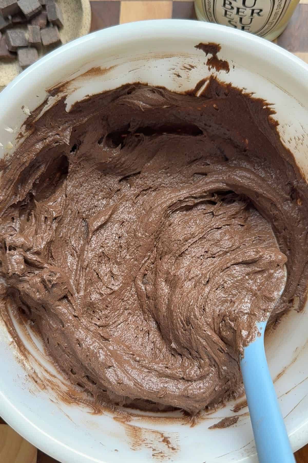 Chocolate muffin batter in a mixing bowl with a rubber spatula.