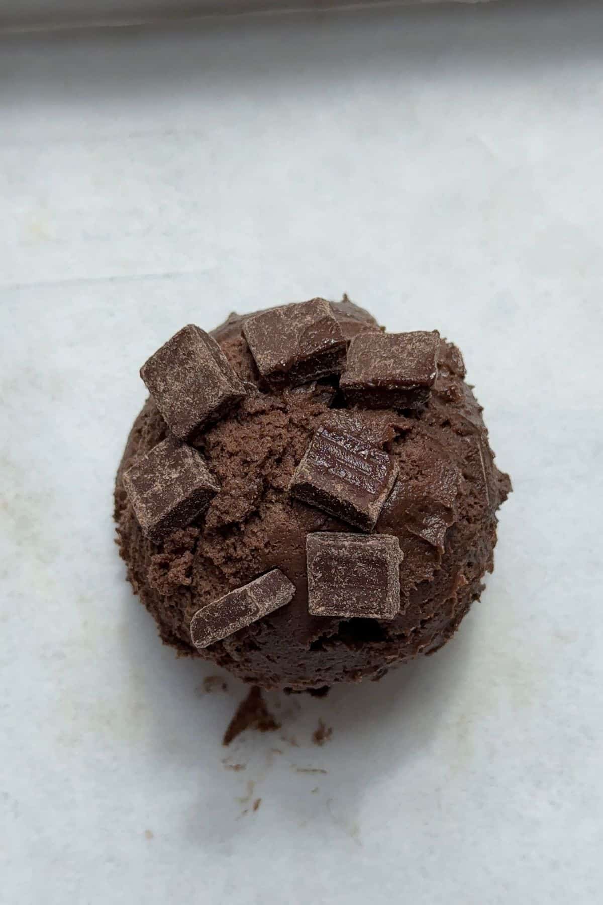An unbaked muffin top with chocolate chunks on parchment paper.