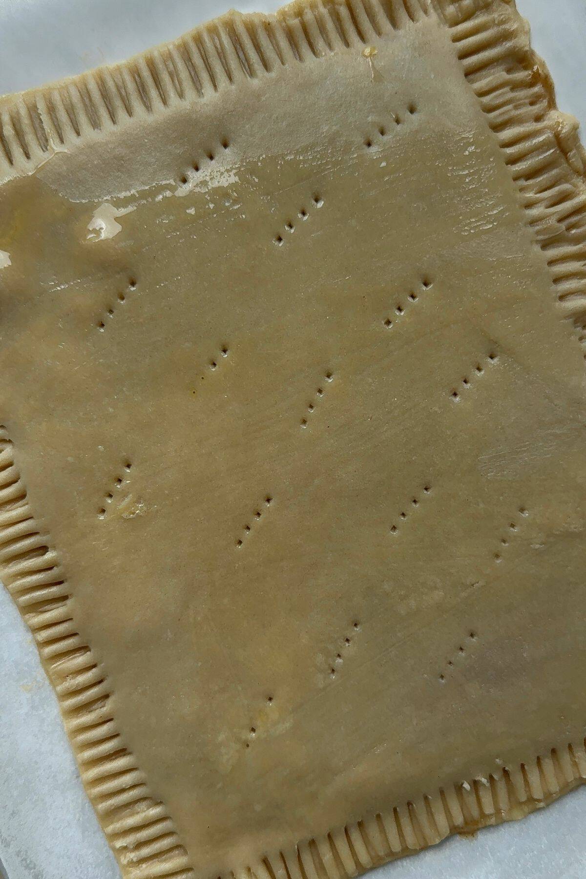 An unbaked rectangle pastry with crimped edges and air holes poked in the center.