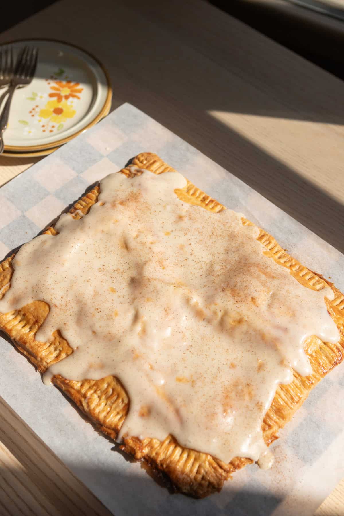A giant banana bread pop tart with cinnamon cream cheese icing on parchment paper.
