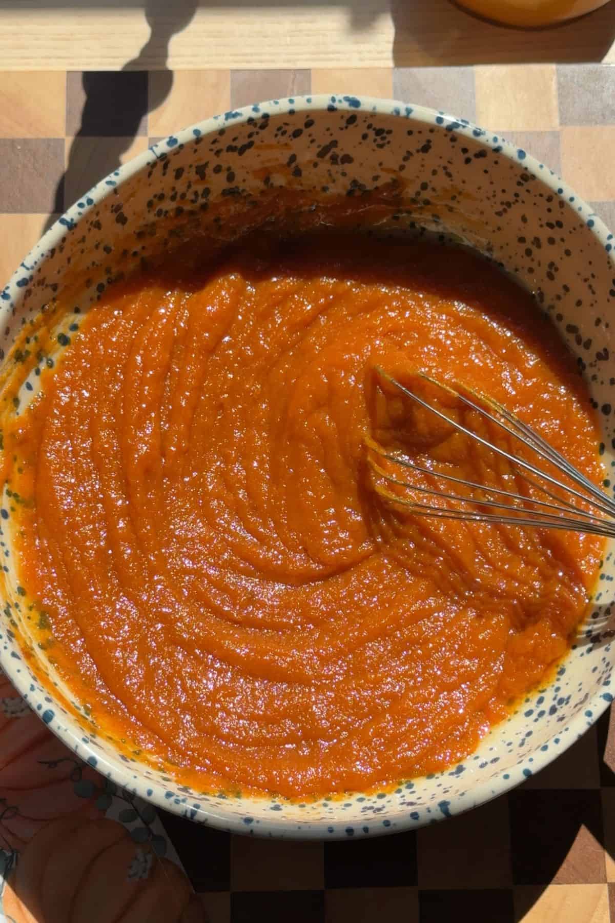 Pumpkin, sugars, and oil whisked together in a large blue speckled bowl.