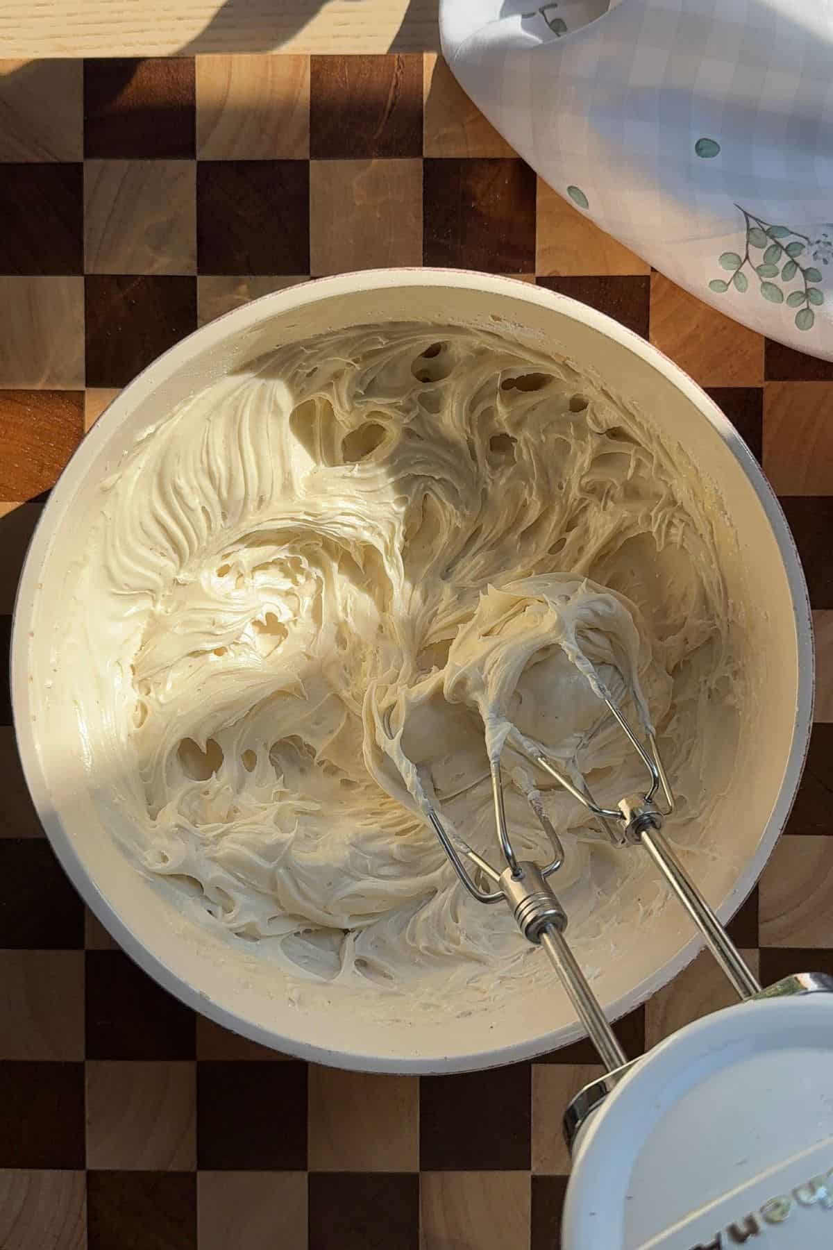 Cream cheese frosting in a bowl with an electric mixer.