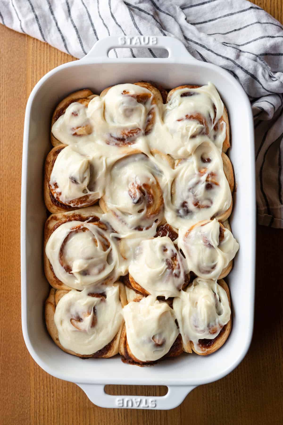 Apple butter cinnamon rolls in a white dish with cream cheese frosting.