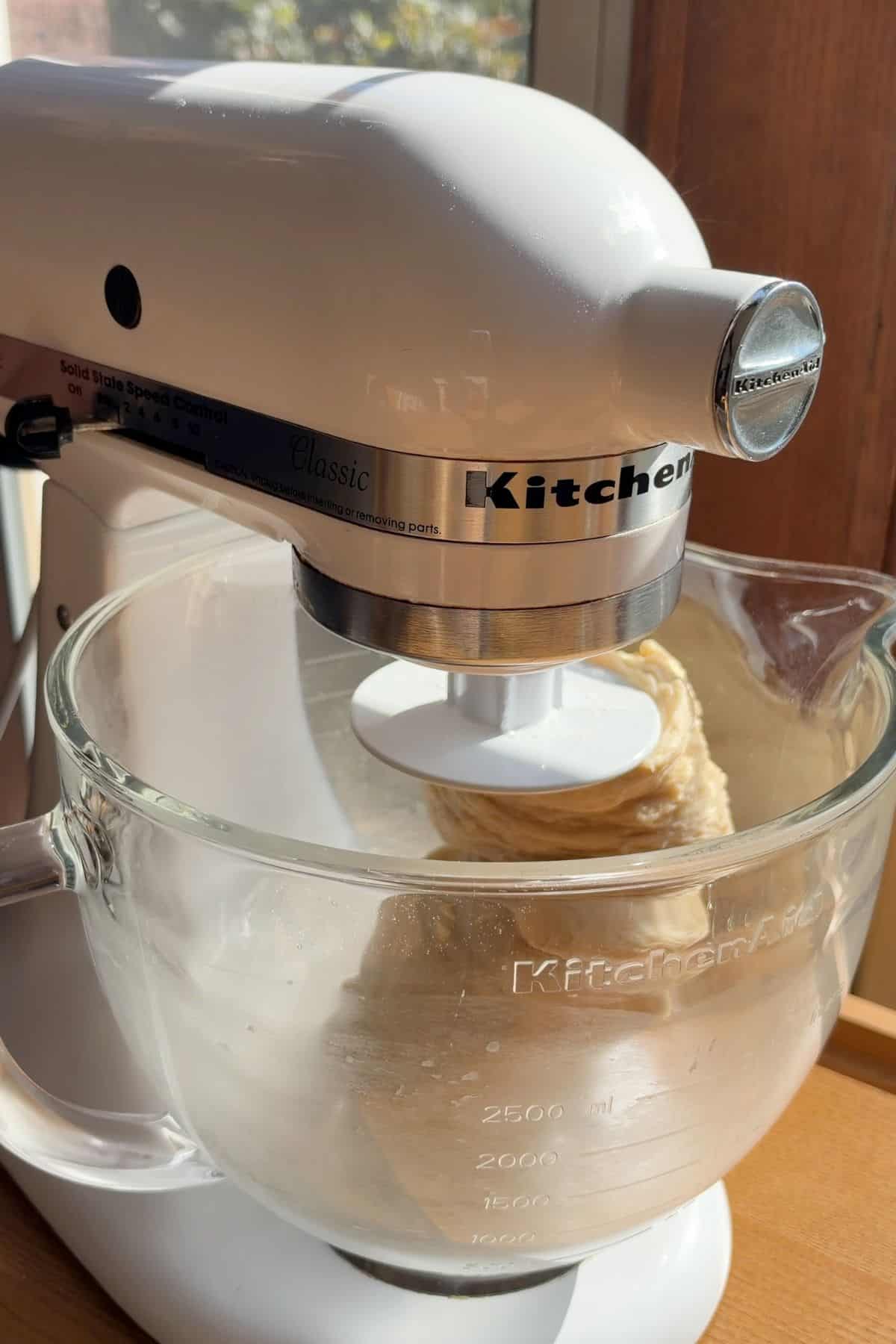 Dough being kneaded in a stand mixer with a dough hook.