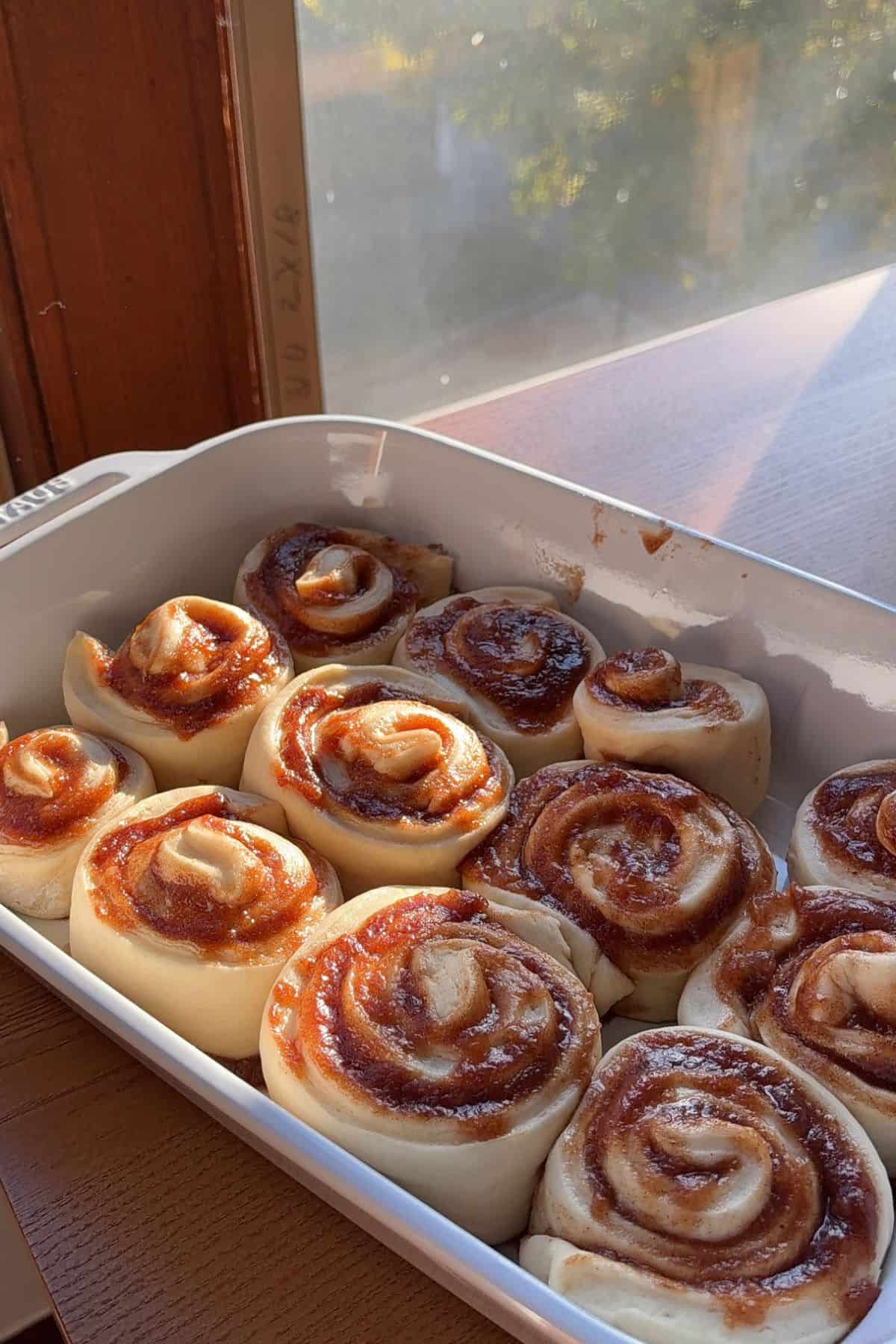 Unbaked cinnamon rolls filled with apple butter in a white baking dish.